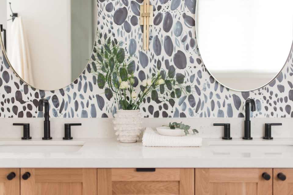 blue stone-look wallpaper in bathroom with gold accents, wood cabinetry, and ceramic decor